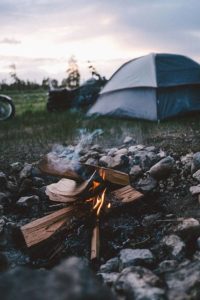Sitting next to campfire with motorcycle and tent in background